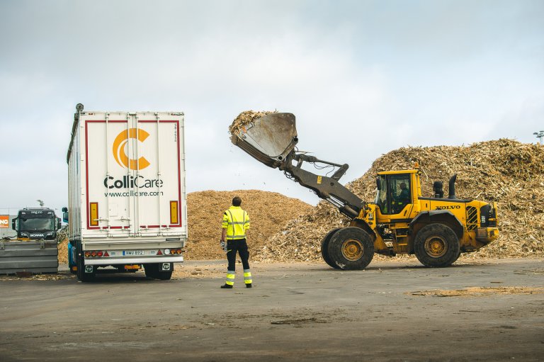 En märkt ColliCare-trailer med rörligt golv som lastas med sågspån av en traktor
